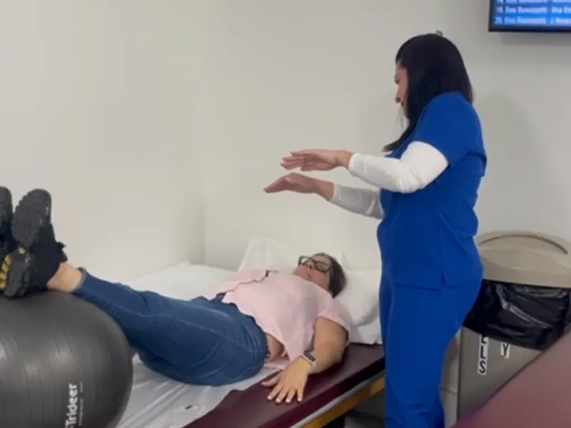 Physical therapist guiding a core and balance exercise with a stability ball at All In One Specialty Health